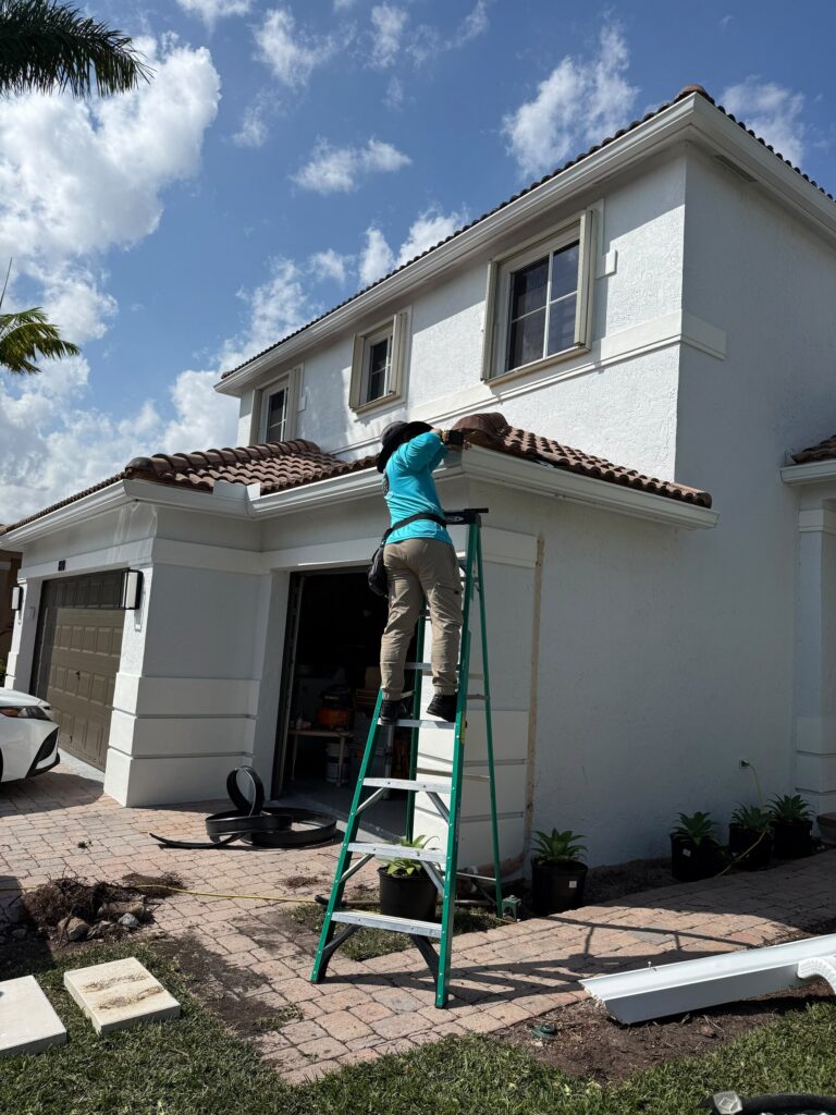 Installer on a ladder clearing and checking a gutter run