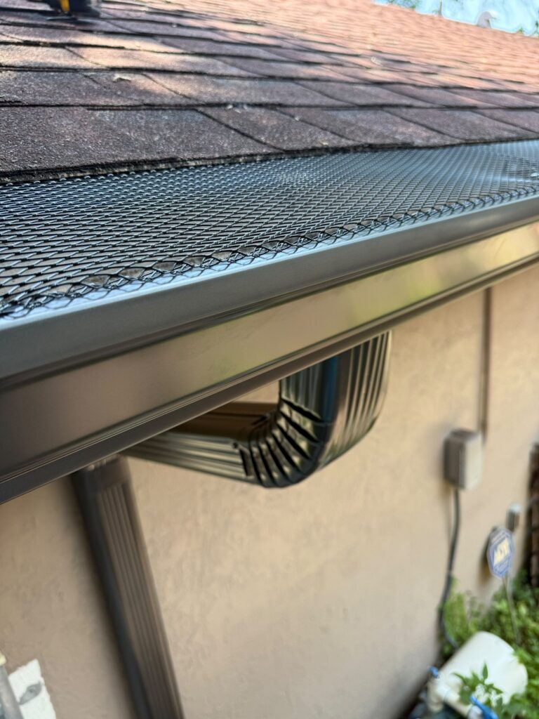 Mesh gutter guard fitted over a gutter on a shingle roof